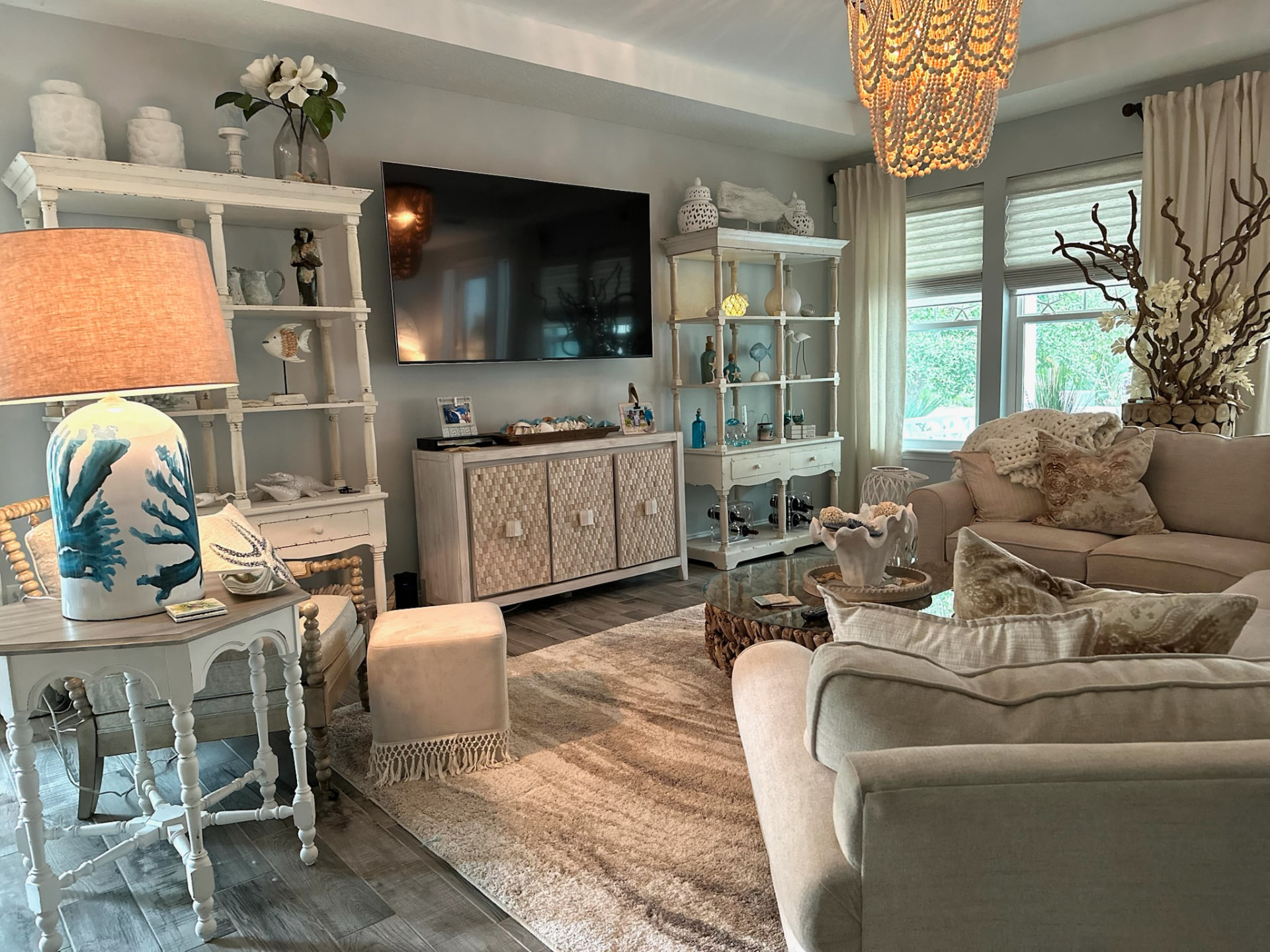 Coastal-inspired living room with neutral sofas, coral-print lamp, woven accents, and curated shelving