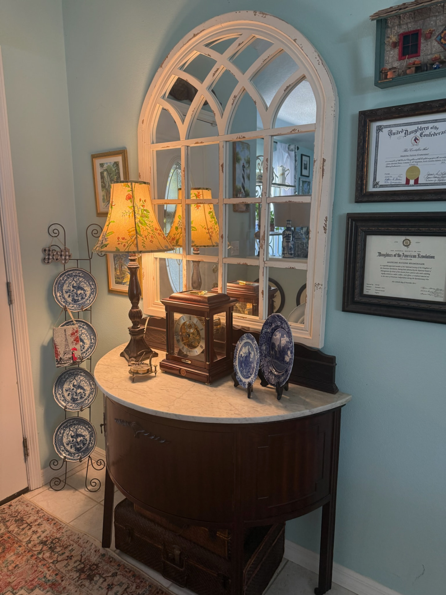 Console table vignette with an arched window-pane mirror, blue-and-white china plates, and a warmly lit lamp