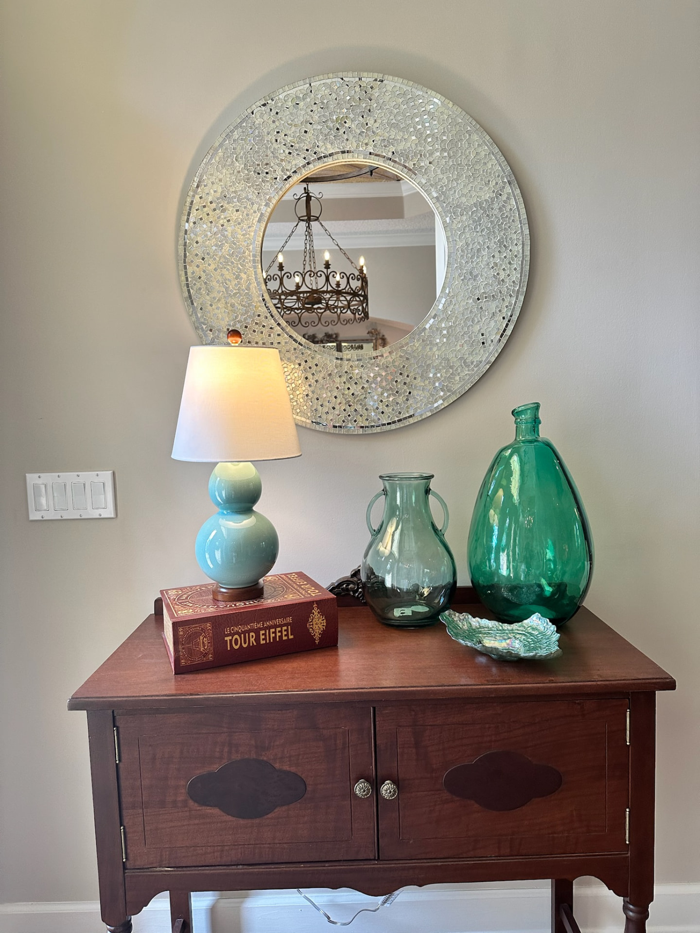 Entry console styled with a mosaic mirror, turquoise gourd lamp, and green glass vessels